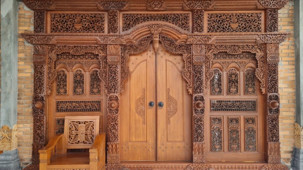 Porte en bois finement sculptée avec des panneaux décoratifs et une chaise en bois assortie sur le côté gauche.