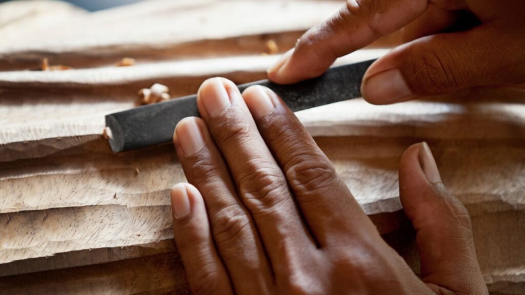 Gros plan de mains utilisant une lime pour lisser une surface en bois avec des rainures sculptées.