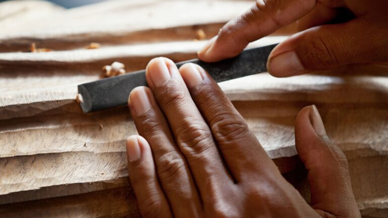 Gros plan de mains utilisant une lime pour lisser une surface en bois avec des rainures sculptées.