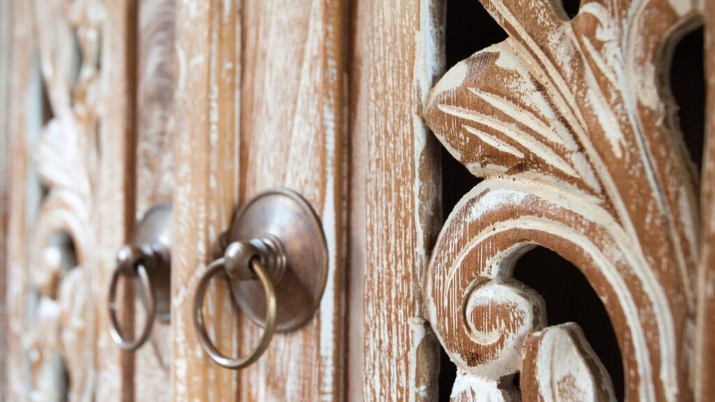 Gros plan de sculptures en bois ornées et de poignées en anneau métallique sur une porte en bois vintage.