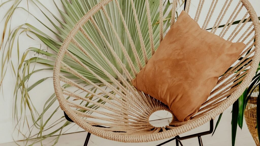 Une chaise en osier avec un coussin beige se trouve devant une grande feuille de palmier verte.