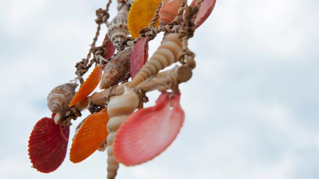 Carillon éolien en coquillage coloré suspendu contre un ciel nuageux.