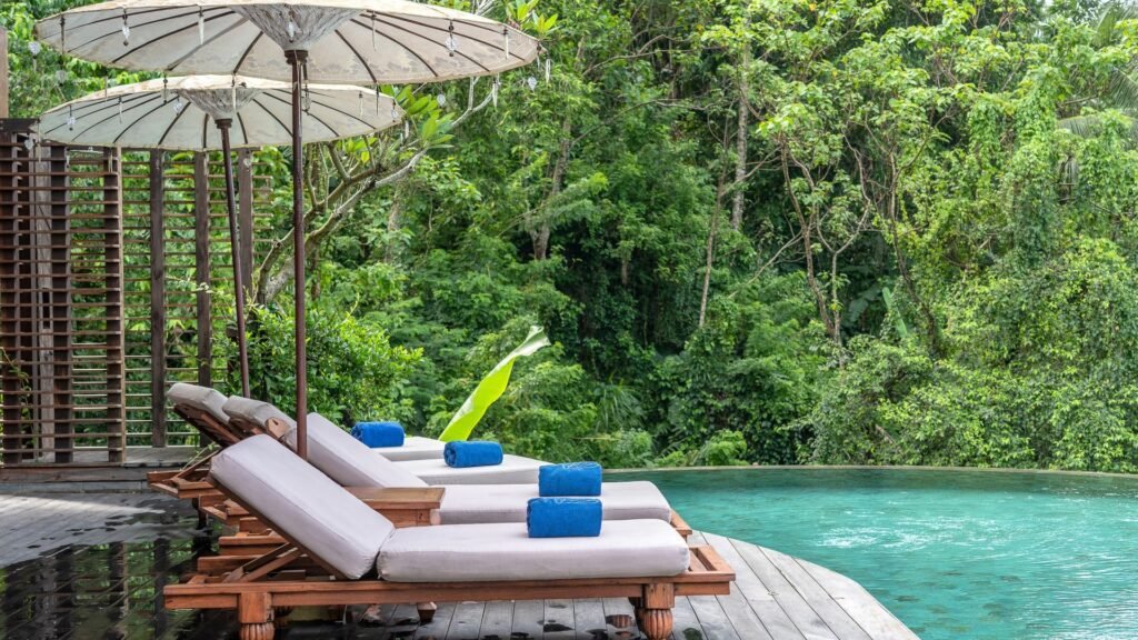 Chaises longues avec serviettes bleues au bord d'une piscine, entourées d'une végétation luxuriante et de grands parasols.
