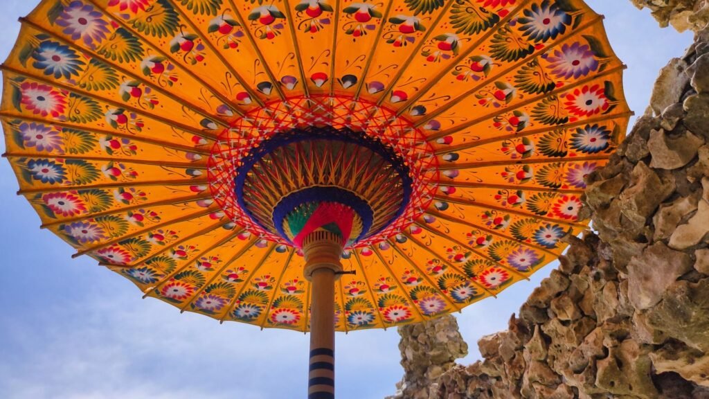 Parasol coloré aux motifs floraux vu d'en bas sur fond de ciel bleu et de rochers.