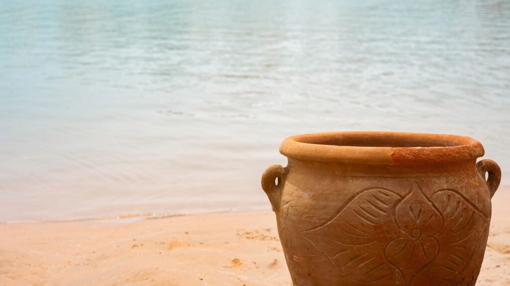 Pot en argile avec un motif floral sur une plage de sable près d'une eau calme.