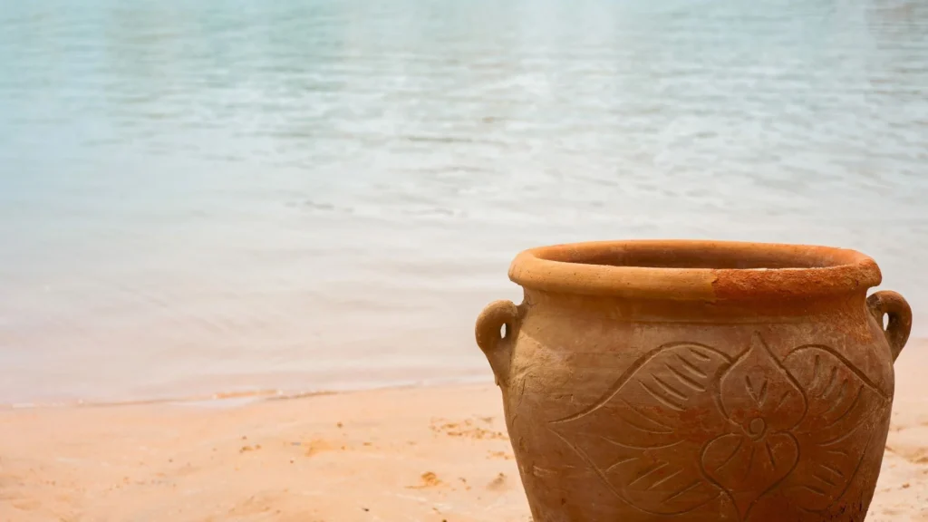 Pot en argile avec un motif floral sur une plage de sable près d'une eau calme.