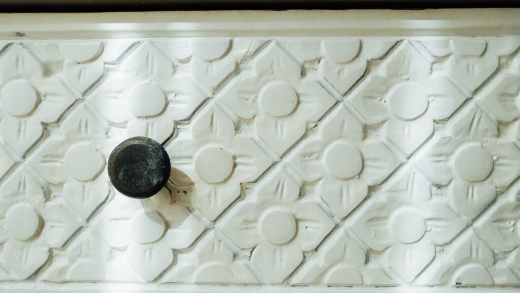 Gros plan d'une surface d'armoire blanche texturée avec des motifs floraux et un seul bouton rond noir.