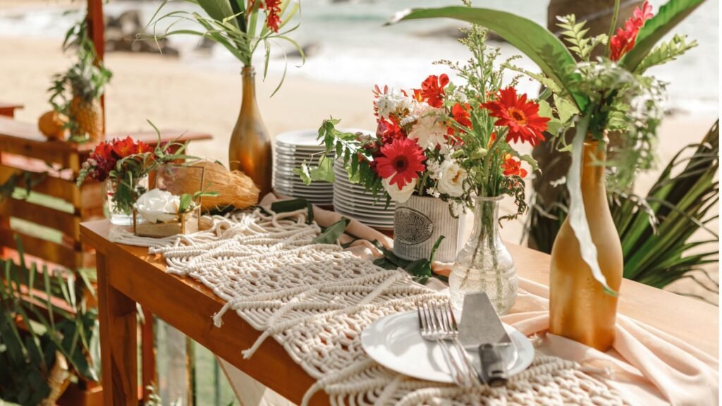 Table de plage avec fleurs, assiettes et décoration tropicale. Vue sur l'océan en arrière-plan.