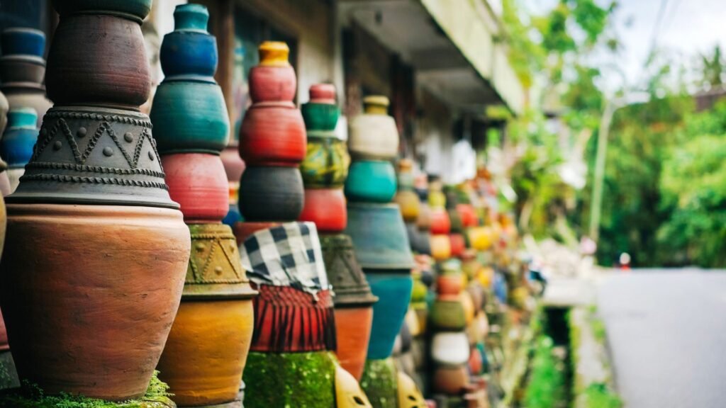 Des pots en argile colorés empilés bordent une route, avec de la verdure et un arrière-plan flou.