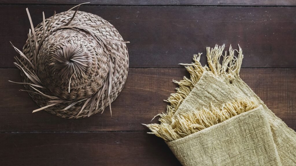 Chapeau de paille tissé et tissu jaune à franges sur une surface en bois.