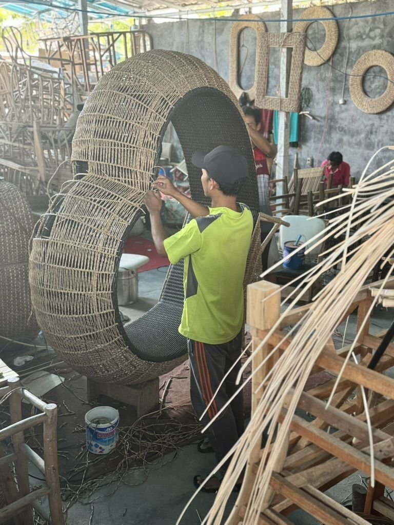 Dans un atelier, une personne tisse des brins de rotin sur le cadre d'une grande chaise de forme ovale