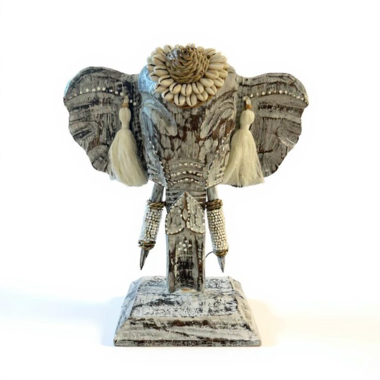 Décoration tête éléphant avec pampilles et coquillages, posée sur une base en bois rustique. Cette décoration murale apporte une touche artisanale unique à votre intérieur.