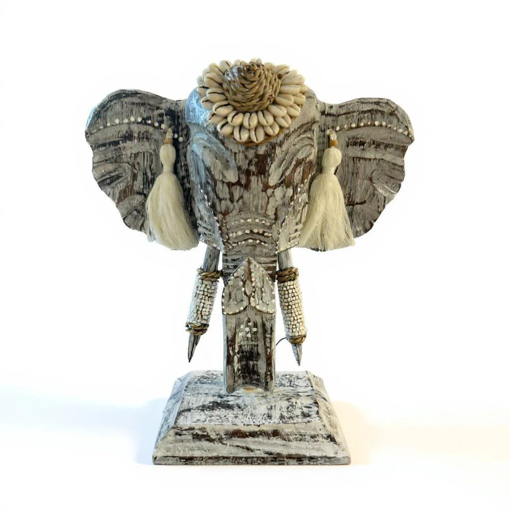Décoration tête éléphant avec pampilles et coquillages, posée sur une base en bois rustique. Cette décoration murale apporte une touche artisanale unique à votre intérieur.